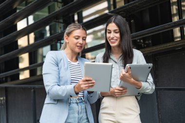 Kurumsal profesyonellerden oluşan çeşitli bir ekip dışarıda iş birliği yapıyor, modern cam ofis binası önünde dizüstü bilgisayardaki verileri analiz ederken stratejik tartışmalara girişiyorlar..
