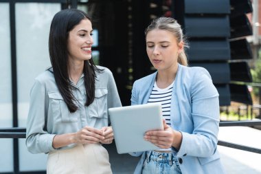 Kurumsal profesyonellerden oluşan çeşitli bir ekip dışarıda iş birliği yapıyor, modern cam ofis binası önünde dizüstü bilgisayardaki verileri analiz ederken stratejik tartışmalara girişiyorlar..