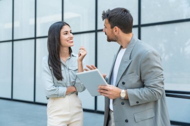 Kurumsal profesyonellerden oluşan çeşitli bir ekip dışarıda iş birliği yapıyor, modern cam ofis binası önünde dizüstü bilgisayardaki verileri analiz ederken stratejik tartışmalara girişiyorlar..