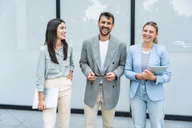 Modern cam ofis binası önünde dizüstü bilgisayardaki verileri analiz ederken dışarıda iş birliği yapan kurumsal profesyonellerden oluşan çeşitli iş adamları..