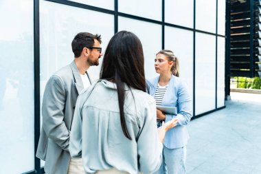 Modern cam ofis binası önünde dizüstü bilgisayardaki verileri analiz ederken dışarıda iş birliği yapan kurumsal profesyonellerden oluşan çeşitli iş adamları..