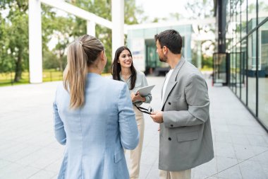 Modern cam ofis binası önünde dizüstü bilgisayardaki verileri analiz ederken dışarıda iş birliği yapan kurumsal profesyonellerden oluşan çeşitli iş adamları..