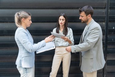 Modern cam ofis binası önünde dizüstü bilgisayardaki verileri analiz ederken dışarıda iş birliği yapan kurumsal profesyonellerden oluşan çeşitli iş adamları..