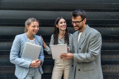 Modern cam ofis binası önünde dizüstü bilgisayardaki verileri analiz ederken dışarıda iş birliği yapan kurumsal profesyonellerden oluşan çeşitli iş adamları..
