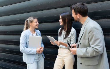 Modern cam ofis binası önünde dizüstü bilgisayardaki verileri analiz ederken dışarıda iş birliği yapan kurumsal profesyonellerden oluşan çeşitli iş adamları..