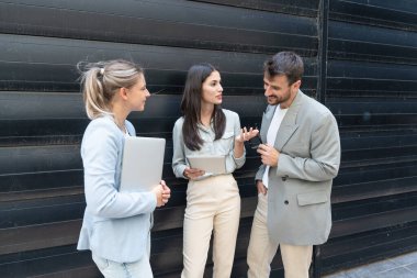 Modern cam ofis binası önünde dizüstü bilgisayardaki verileri analiz ederken dışarıda iş birliği yapan kurumsal profesyonellerden oluşan çeşitli iş adamları..