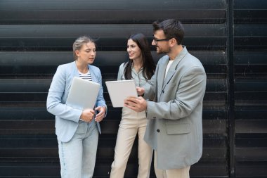 Modern cam ofis binası önünde dizüstü bilgisayardaki verileri analiz ederken dışarıda iş birliği yapan kurumsal profesyonellerden oluşan çeşitli iş adamları..