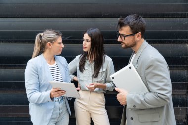 Modern cam ofis binası önünde dizüstü bilgisayardaki verileri analiz ederken dışarıda iş birliği yapan kurumsal profesyonellerden oluşan çeşitli iş adamları..