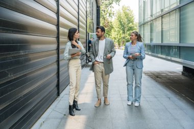 Modern cam ofis binası önünde dizüstü bilgisayardaki verileri analiz ederken dışarıda iş birliği yapan kurumsal profesyonellerden oluşan çeşitli iş adamları..