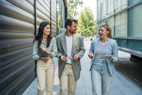 Modern cam ofis binası önünde dizüstü bilgisayardaki verileri analiz ederken dışarıda iş birliği yapan kurumsal profesyonellerden oluşan çeşitli iş adamları..