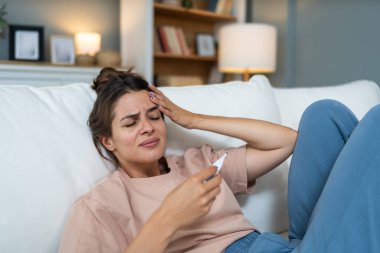 Yüksek vücut ısısı ve baş ağrısı olan, termometreyi tutan genç, sinirli ve endişeli bir kadın. Çünkü düğününe birkaç gün kaldı. Müstakbel gelin üşütmüş ve grip olmuş.