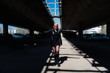 Deri ceketli, koyu kırmızı güneş gözlüklü, modern şehir ortamında kendine güvenen sokak modacı kız. Özgürlük kavramı