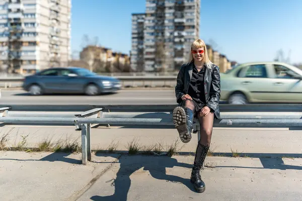 Deri ceketli, koyu kırmızı güneş gözlüklü, modern şehir ortamında kendine güvenen sokak modacı kız. Özgürlük kavramı