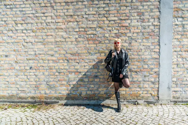 Deri ceketli, koyu kırmızı güneş gözlüklü, modern şehir ortamında kendine güvenen sokak modacı kız. Özgürlük kavramı