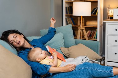 Yorgun anne, kucağında dinlenen küçük kızına masal okurken uykuya dalıyor. Oturma odasındaki kanepede sıcak, sevgi ve akşam sükunetiyle huzurlu bir şekilde dinleniyor.