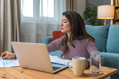 Genç kadın serbest çalışan küçük bir şirket sahibi dizüstü bilgisayarında verilerle vergi iadesi hesaplıyor. İç işlerinde çalışmak, profesyonel meslekte kadın modern teknoloji kullanıcısı..