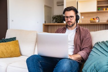 Genç iş adamı küçük bir şirket sahibi, evde çalışıyor, grafikleri ve dizüstü bilgisayarları kontrol ediyor. Yeni ürün stratejisinin maliyetlerini ve giderlerini hesaplayan yenilikçi genç serbest erkek.