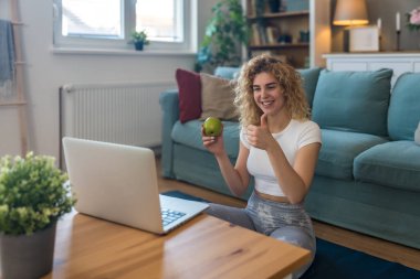 Spor kıyafetli genç bir kadın evde spor yapıyor, bilgisayar ekranından sanal antrenörü takip ediyor, çevrimiçi egzersiz oturumuna odaklanıyor, rutin, motivasyon ve sağlıklı yaşam tarzını sürdürüyor.