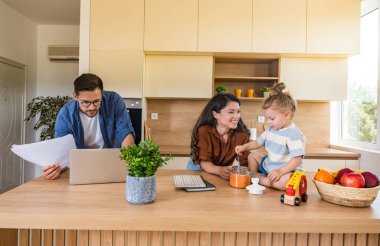 Neşeli genç aile, modern mutfak anne ve kızıyla kaynaşıyor. Tezgahta oynarken gülüyorlar. Babası uzak işlere odaklanıyor, ebeveynlik, sevgi ve teknolojiyi harmanlıyor. Basit yaşam.