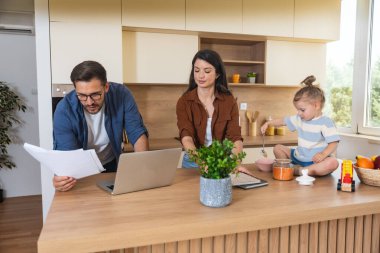 Neşeli genç aile, modern mutfak anne ve kızıyla kaynaşıyor. Tezgahta oynarken gülüyorlar. Babası uzak işlere odaklanıyor, ebeveynlik, sevgi ve teknolojiyi harmanlıyor. Basit yaşam.