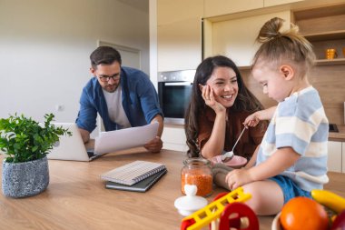 Neşeli genç aile, modern mutfak anne ve kızıyla kaynaşıyor. Tezgahta oynarken gülüyorlar. Babası uzak işlere odaklanıyor, ebeveynlik, sevgi ve teknolojiyi harmanlıyor. Basit yaşam.