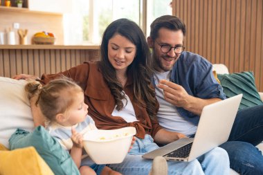 Mutlu, genç bir aile evlerinde kanepede oturup dizüstü bilgisayarda internet üzerinden internet üzerinden tatil beldesi arıyor ve küçük çocuklarıyla seyahat ediyorlar. Eğlence arayan çocuk ebeveynler.