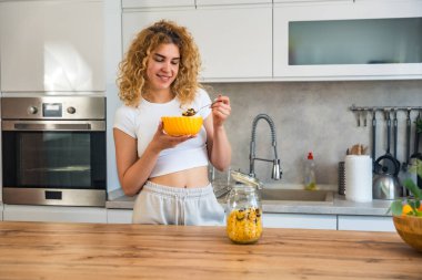 Mutfakta kahvaltı yapan güzel bir genç kadının portresi. Sağlıklı bir vücut ve sağlık için sabah yulaf ezmesi yiyen bir kız için sağlıklı bir diyet. Olumlu düşün, iyi beslen ve akıllı ol..