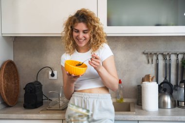 Mutfakta kahvaltı yapan güzel bir genç kadının portresi. Sağlıklı bir vücut ve sağlık için sabah yulaf ezmesi yiyen bir kız için sağlıklı bir diyet. Olumlu düşün, iyi beslen ve akıllı ol..