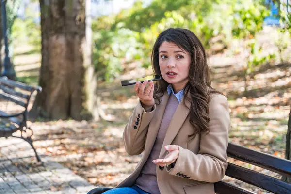 Telefon görüşmesi sırasında parktaki bankta oturan zarif iş kadını, farklı duyguları ifade ediyor mutluluk, öfke, sakinlik, açık hava kentsel ortamında iş molasında birden fazla iş. Ofis çalışanı dışarıda..