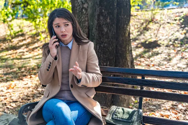 Telefon görüşmesi sırasında parktaki bankta oturan zarif iş kadını, farklı duyguları ifade ediyor mutluluk, öfke, sakinlik, açık hava kentsel ortamında iş molasında birden fazla iş. Ofis çalışanı dışarıda..