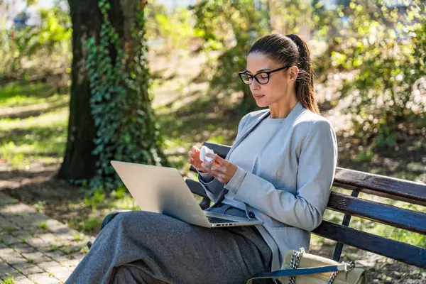 Parktaki bankta oturan profesyonel bir kadın, bilgisayar işine odaklanmış iş arkadaşlarıyla görüntülü konuşma, verimlilik işi modern uzaktan kumandalı, dijital göçebe yaşam tarzı ve kentsel sükunet