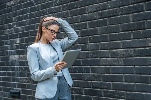 Modern ofis binasının dışında kendine güvenen profesyonel bir kadın dijital tabletle etkileşimde bulunuyor, dinamik bir iş ortamında odak, yenilik ve kentsel kurumsal yaşam tarzını gösteriyor.