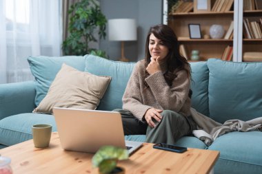 Oturma odasından online terapi seansına katılan genç bir kadın, profesyonel bir terapist, zihinsel sağlık ve kişisel gelişim desteği ile dijital iletişim yoluyla konuşurken duygularını ifade ediyor..