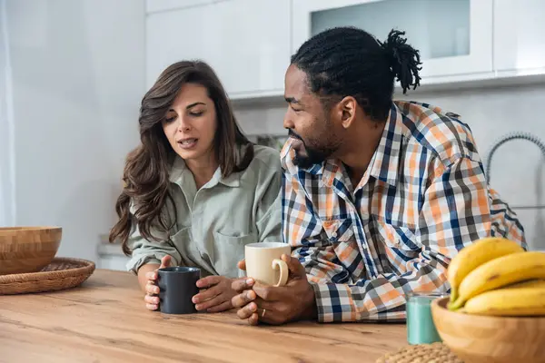 Mutlu çift yeni evlerinin mutfağında kahvenin tadını çıkarıyorlar. Birlikte rahat bir sabah geçiriyorlar. Rahatlamış ve gülümsüyorlar.