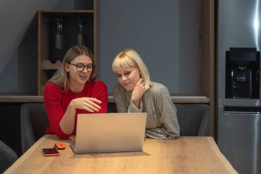 Şarap imalathanesinde pazarlama stratejisi üzerinde çalışan iki profesyonel iş kadını, laptopa odaklanmış, pozitif enerji, markalaşma fikirleri ve üzüm bağı görselleri ile çevrili..