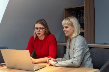 Şarap imalathanesinde pazarlama stratejisi üzerinde çalışan iki profesyonel iş kadını, laptopa odaklanmış, pozitif enerji, markalaşma fikirleri ve üzüm bağı görselleri ile çevrili..