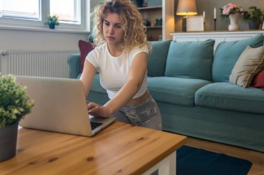 Uzun çalışma saatlerinden kalan sırt ağrısını hafifletmek için evde egzersiz yapan genç kız öğrenci, dizüstü bilgisayarın yanında otururken online egzersiz programları kullanarak, sağlık ve duruş gelişimi üzerine odaklanarak,