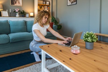 Uzun çalışma saatlerinden kalan sırt ağrısını hafifletmek için evde egzersiz yapan genç kız öğrenci, dizüstü bilgisayarın yanında otururken online egzersiz programları kullanarak, sağlık ve duruş gelişimi üzerine odaklanarak,
