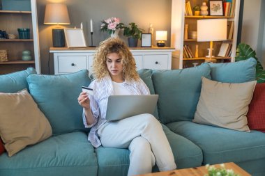 Evde elinde kredi kartı olan ve bilgisayarını online alışveriş, finansal planlama, seyahat rezervasyonu veya banka hesabı, rahat dijital yaşam tarzı ve e-ticaret konsepti için kullanan genç bir kadın.