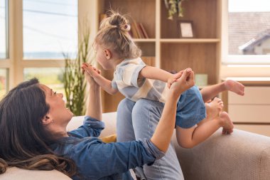 Bekar anne ve küçük kızı evde uçak oyunu oynuyor. Sevgi dolu, neşeli, çocuk ve ebeveyn arasındaki yaratıcı etkileşim, sıcak, güneşli bir oturma odasında güven ve güçlü aile bağları kurmak.