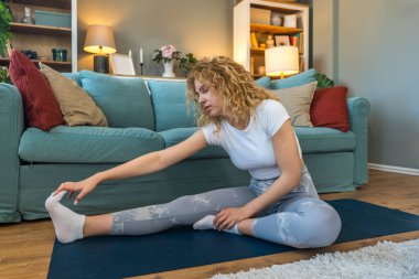 Ciddi bir araba kazasından sonra iyileşen genç bir kadın, kaslarını esneten, yoga minderi üzerinde rehabilitasyon egzersizleri yapan, bina dayanıklılığı, esneklik ve kapalı alanda esneklik sağlayan bir kadın.