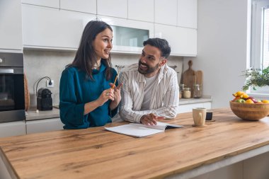 Genç nişanlı çift modern mutfaklarında bir arada duruyorlar, düğün için konuk listesi hazırlıyorlar, yemek menüleri düzenliyorlar, odaklanıyorlar ve gülümsüyorlar.