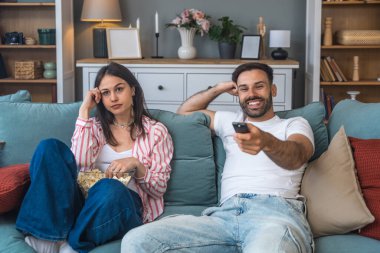 Genç bir çift, ilk randevu gecesi evlerinde kanepede oturup spor veya film izlerken, erkek tamamen meşgul ve heyecanlı, kadın ise sıkılmış ve ilgisiz görünüyor, sessizce patlamış mısır yiyor.