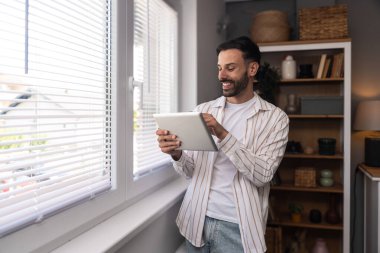 Ofiste dijital tablet üzerinde çalışan çekici bir adam. İşadamı küçük bir şirket sahibi dairesinden online olarak çalışıyor. Bağımsız serbest grafik tasarımcı erkek özgürlük ve işin tadını çıkarıyor.