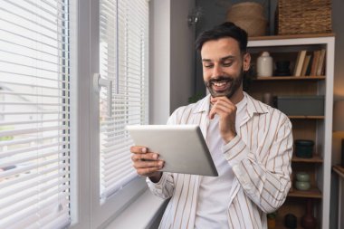 Ofiste dijital tablet üzerinde çalışan çekici bir adam. İşadamı küçük bir şirket sahibi dairesinden online olarak çalışıyor. Bağımsız serbest grafik tasarımcı erkek özgürlük ve işin tadını çıkarıyor.