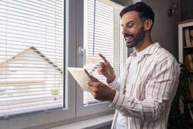 Ofiste dijital tablet üzerinde çalışan çekici bir adam. İşadamı küçük bir şirket sahibi dairesinden online olarak çalışıyor. Bağımsız serbest grafik tasarımcı erkek özgürlük ve işin tadını çıkarıyor.