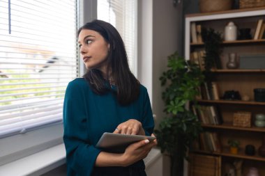Ev ofisinde dijital tablet üzerinde çalışan çekici bir kadın. İş kadını küçük bir şirket sahibi dairesinden internet üzerinden çalışıyor. Bağımsız serbest grafik tasarımcı kadın özgürlük ve işin tadını çıkarıyor.