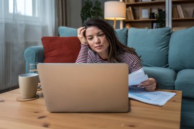 Yerde dizüstü bilgisayar üzerinde çalışırken odaklanma sorunu yaşayan genç bir kadın, basılı analitik, hiperaktivite bozukluğu, zihinsel yorgunluk, tükenmişlik ve modern çoklu görev beklentilerinin baskısı ile mücadele ediyor.