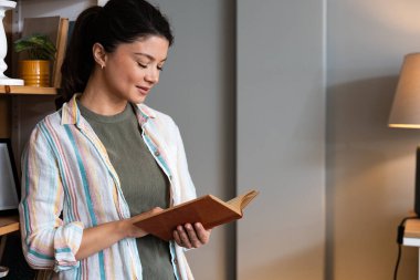 Evde kitap okuyan sakin bir kadın. Huzurlu anların ve boş zamanların tadını çıkarıyor. Edebiyat ve rahatlama ile meşgul, zihinsel berraklık ve duygusal refah için sessiz kapalı aktivite kucaklıyor.