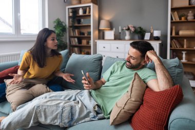Evde akıllı telefon kullanan kıskanç bir kadınla partneri arasındaki ilişki anlaşmazlığı, iletişim sorunlarını, güven sorunlarını, duygusal gerilimi ve çiftlerde dijital dikkat dağınıklığını gösteriyor